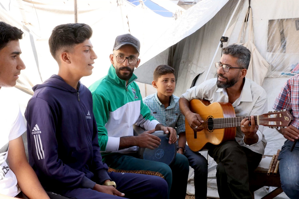 أحمد أبو عمشة محاط بالأطفال لعزف الموسيقى والغناء وتعلم الموسيقى.
